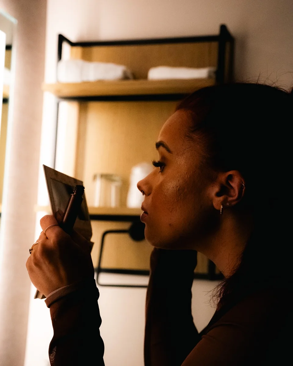 Woman doing her makeup in a hand mirror, lit from the side